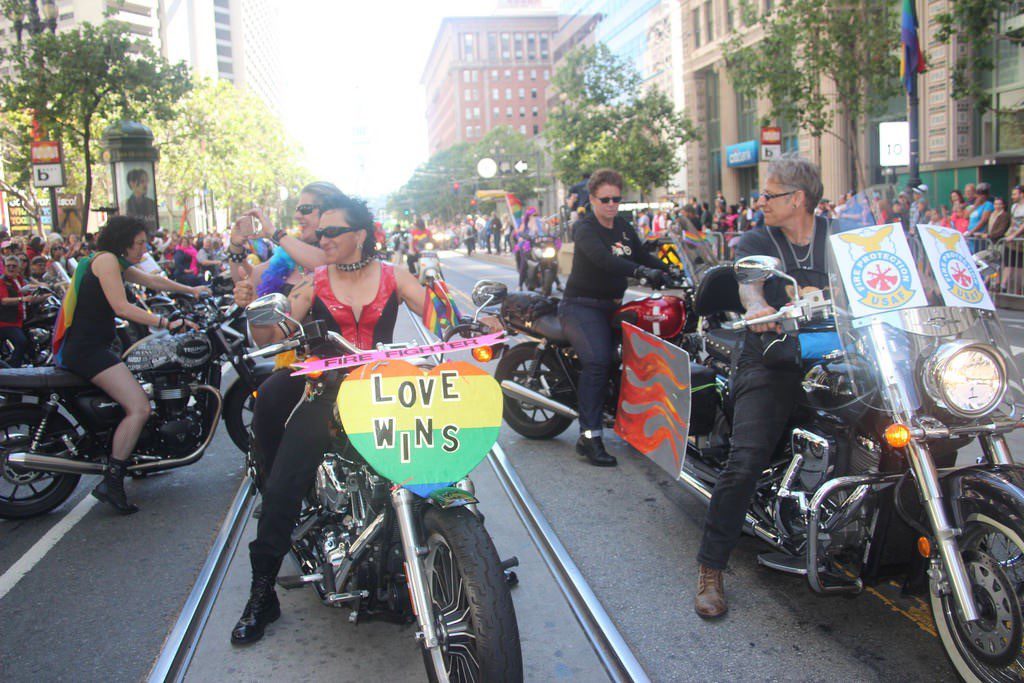 Fig. 2. Malone, Erin. 2016 San Francisco PRIDE Parade Lineup. Many lesbians dressed in black and rainbow colors sit on motorcycles, ready to begin the parade. One has signs on her bike saying "Firefighter" and "Love Wins."