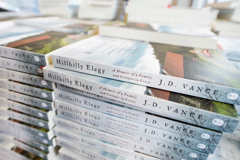 Photo of a stack of books. The spines say “Hillbilly Elegy” by J.D. Vance.