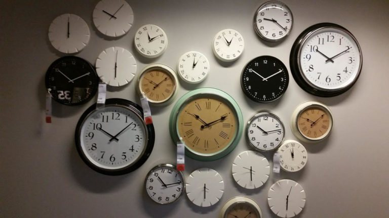 Approximately two dozen different clocks hanging on a wall.