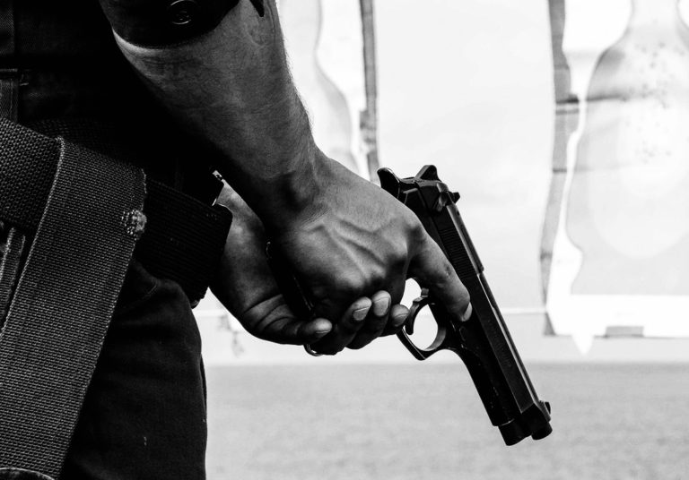 Photo of man's hands holding a handgun pointed down at the ground.