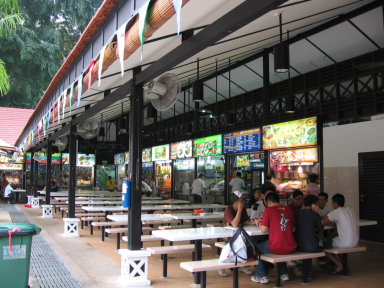 Photo of Newton Food Centre in Singapore. People are eating at tables under a covered area next to restaurants.
