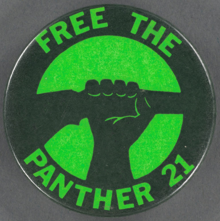 Photo of a green and black button with an illustration of a fist holding up a rifle with "Free the Panther 21" written around the edge.