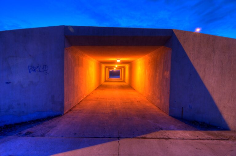 Color photo of an underpass in Bismark, ND illuminated in orange light against a blue sky at twilight.