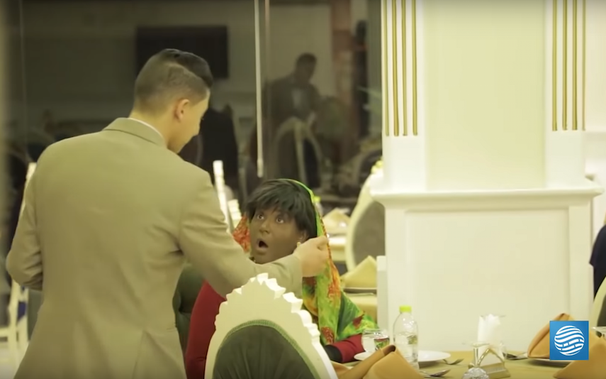 An actress in blackface looks shocked while speaking to a restaurant server.