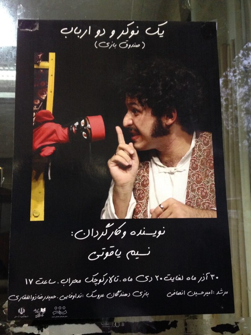 A poster advertising a puppet show at Mehrab theater. The puppet appears with a black face and in a red outfit, and is depicted next to an actor.