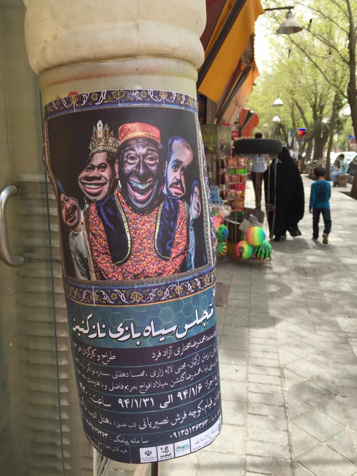 A poster of a theater show in Yazd, Iran, showing the distorted faces of three characters, including one in blackface.