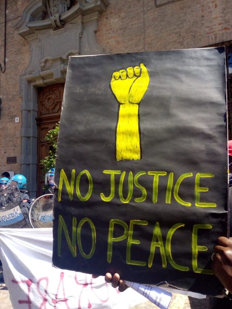Photo of a black protest sign with a yellow raised fist that reads "No justice no peace"