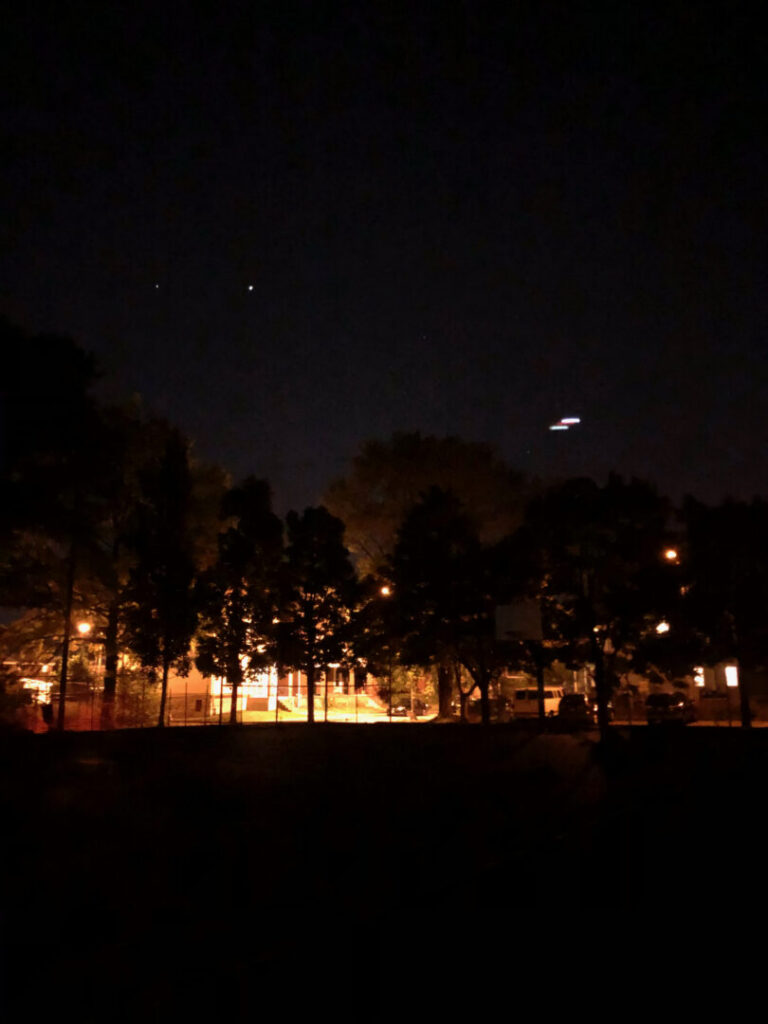 Photo of the night sky, a few stars, a basketball hoop, and lights from the street