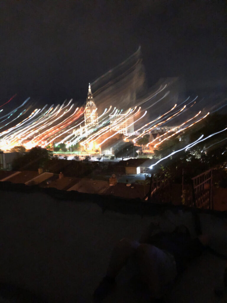 Photo of a city at night taken from a rooftop. The lights are blurred from movement.