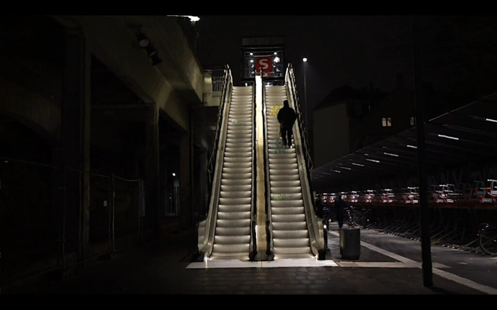 Photo of an escalator illuminated in darkness with a single passenger going up on the right.