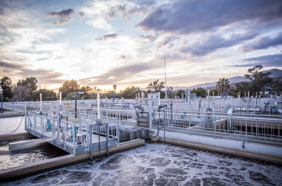 Photo of a water treatment plant framed by rows of railing and walkways is set in the foreground. In the background are palm trees and a sunrise in Santa Barbara, California.