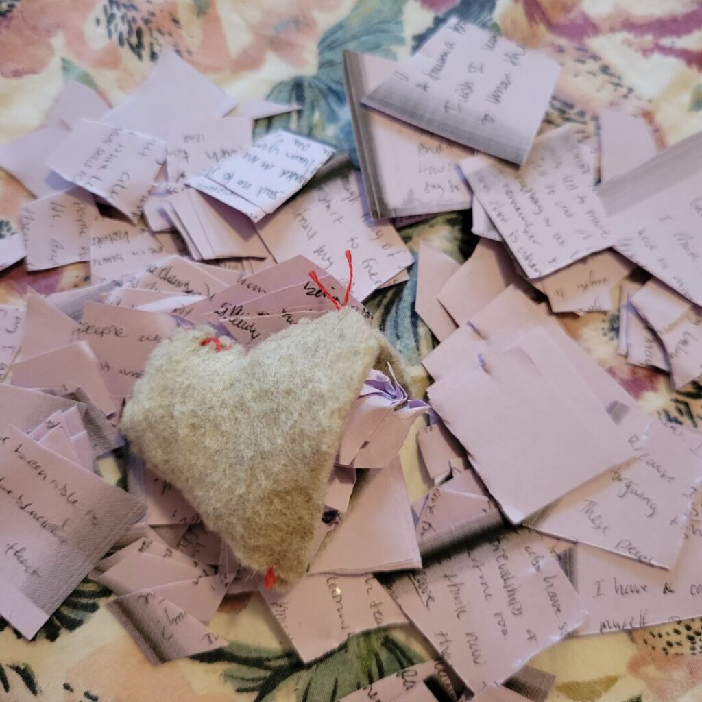 A close up photo of the felt heart being filled with photocopied writing entries from the workbook. These entries are comprised of Sav sharing their story of their abuse.