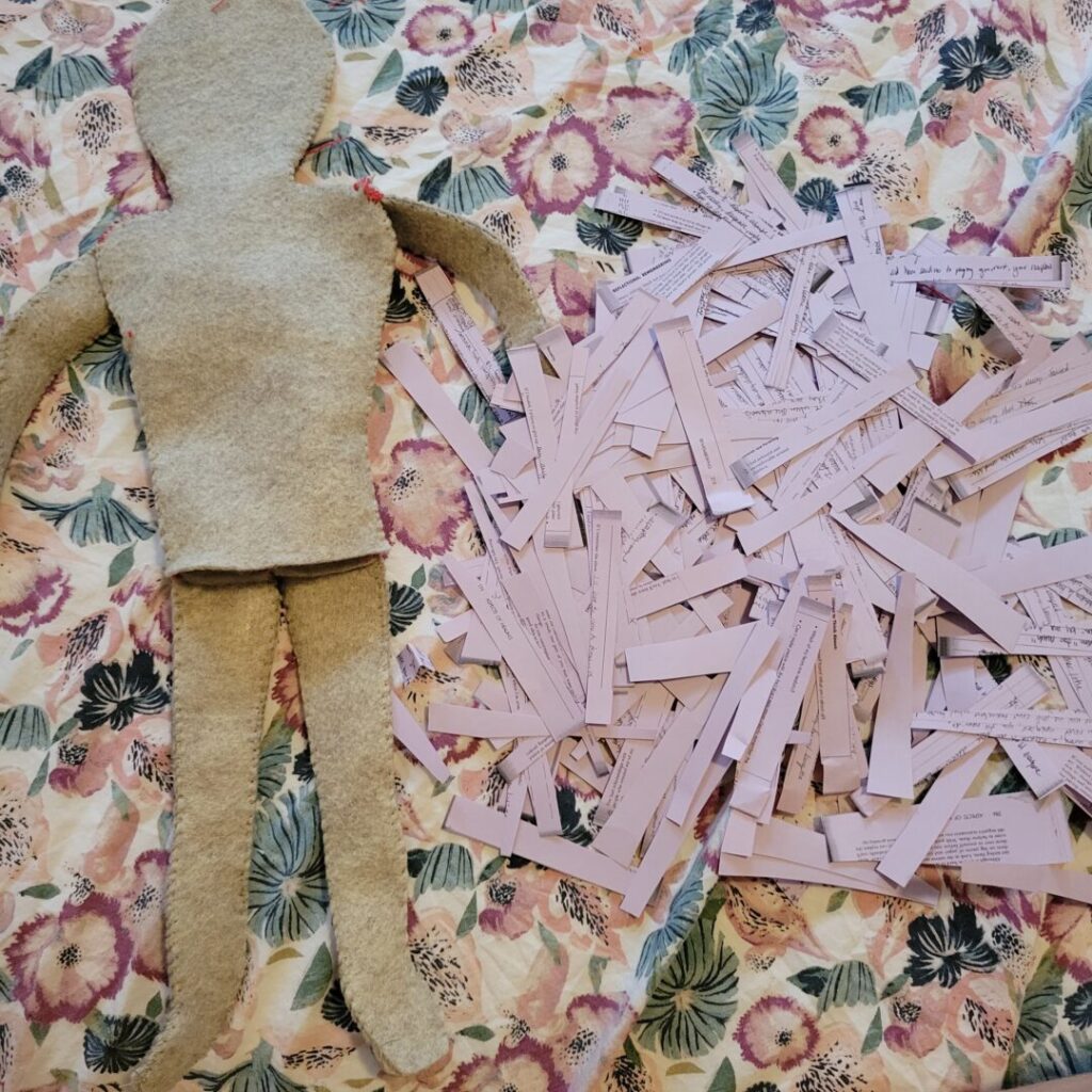 A photo of the felt doll next to shredded pages of the purple photocopied pages of "The Courage to Heal" before being used to fill the cavity of the doll.
