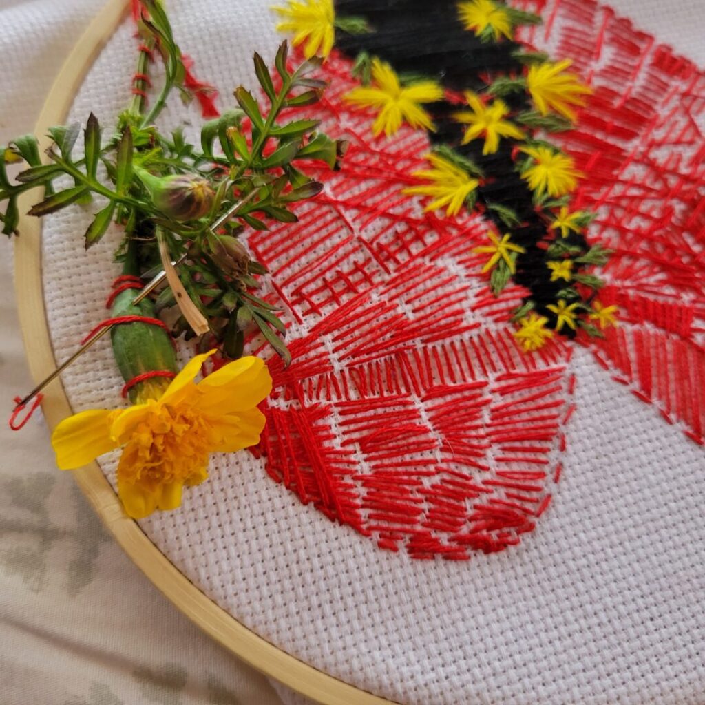 Small yellow flowers have been stitched along the edges of the black thread, and a yellow marigold flower has been sewn next to the heart.
