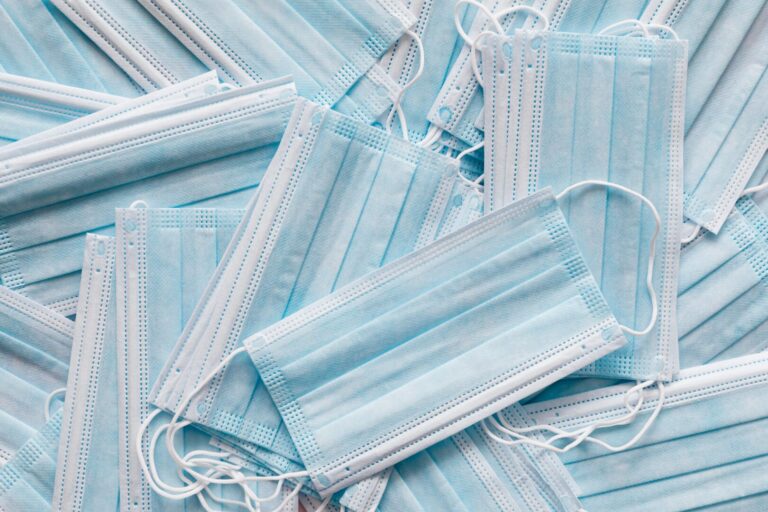 A pile of light blue, unused, disposable surgical masks.