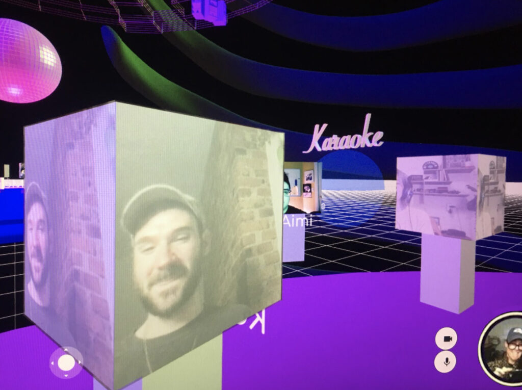 A view from the point-of-view of a participant/avatar in the GlitchRealm, rectangular avatars showing faces navigate the space. They show Kevin Gotkin in the foreground with Yo-Yo Lin and Aimi Hamraie behind them. A purple floor is underneath and a pink disco ball hangs in the upper left corner. The word “karaoke” appears in light pink in the distance, an invitation to enter the karaoke room. Navigation arrows and other icons appear on the screen. In the bottom right corner of the screen is the viewer, moira williams. They appear in a round bubble and are seen taking a photo of their computer screen. Based on their proximity, these avatars would have been able to receive more legible audio from one another than the avatars further away.