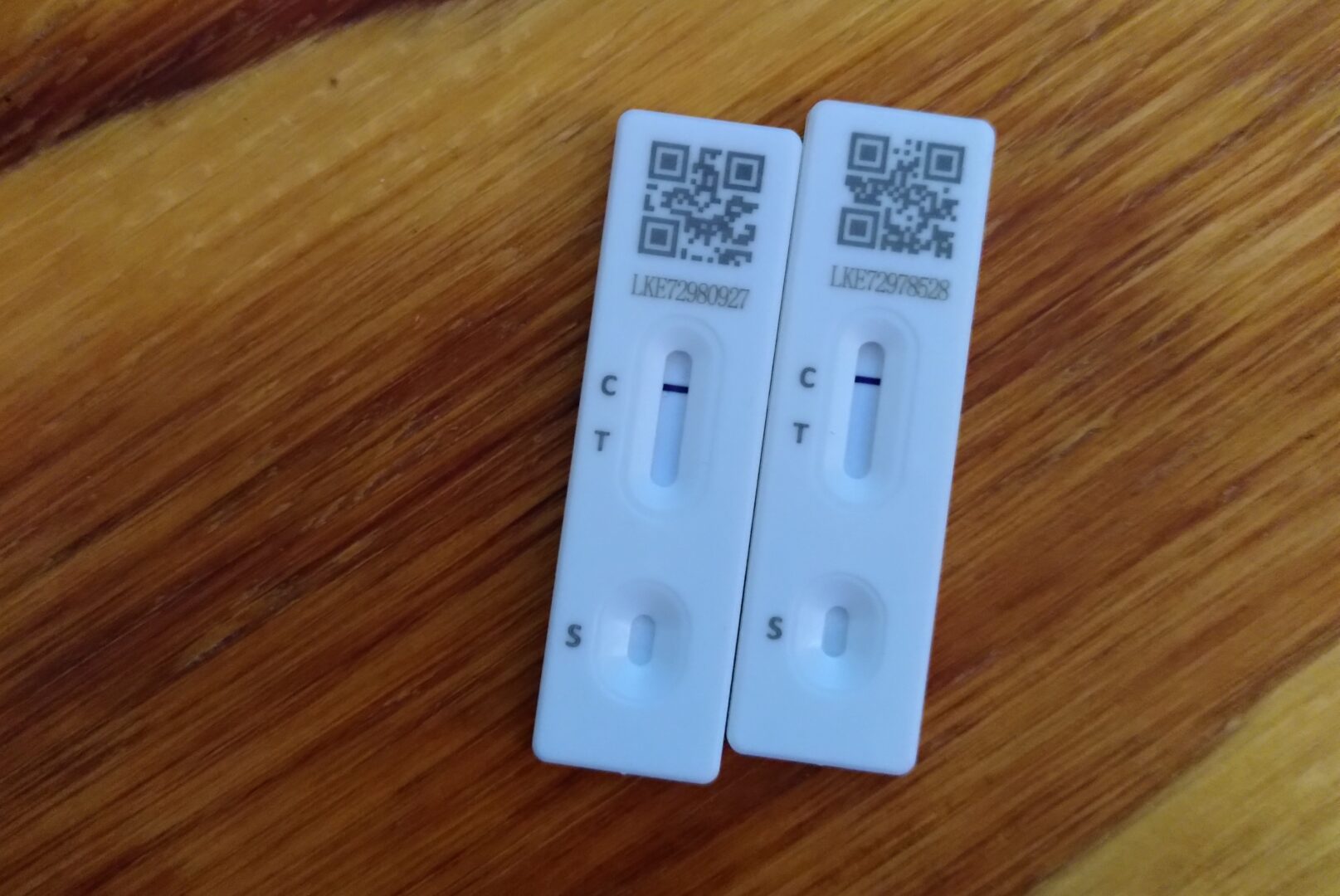 Photo of two negative at-home COVID-19 lateral flow tests, placed close together on a wooden background.