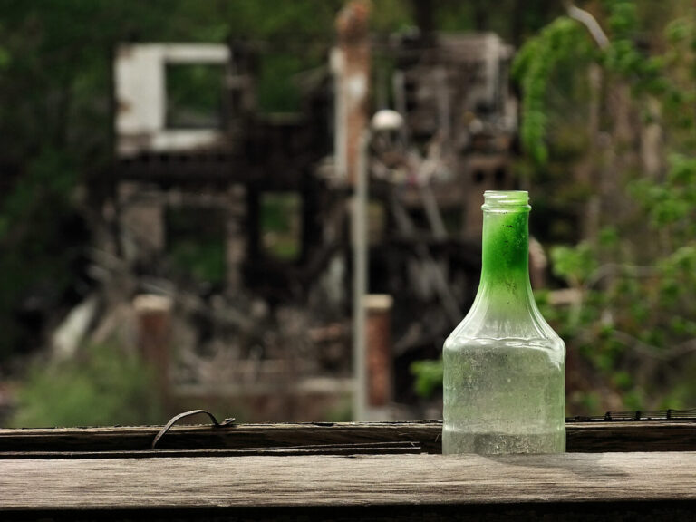 Photo of a bottle sitting on a wooden surface with blurred debris in the background.
