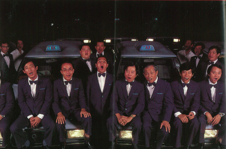 Taxi drivers in suits singing in a choir behind taxi vehicles.