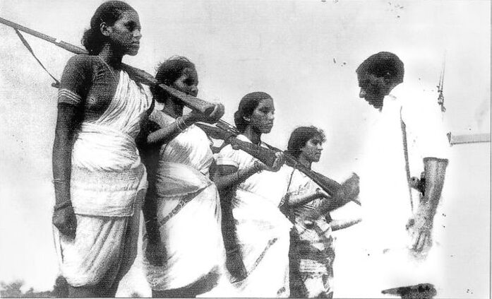 A man stands in front of four women who are holding rifles over their shoulders