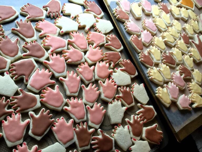 Two trays of cookies shaped like hands in various colors