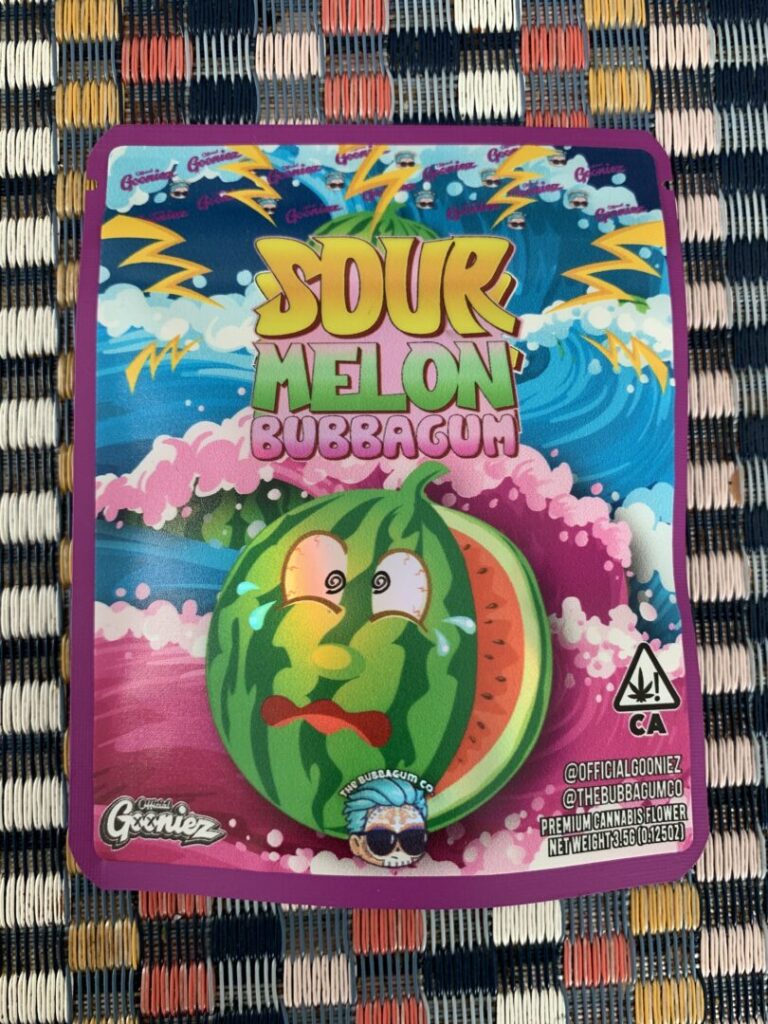 Cannabis package for the “Sour Melon Bubbagum” strain featuring a large anthropomorphic watermelon with eyes and a mouth and with a slice missing, revealing red flesh and black seeds. 