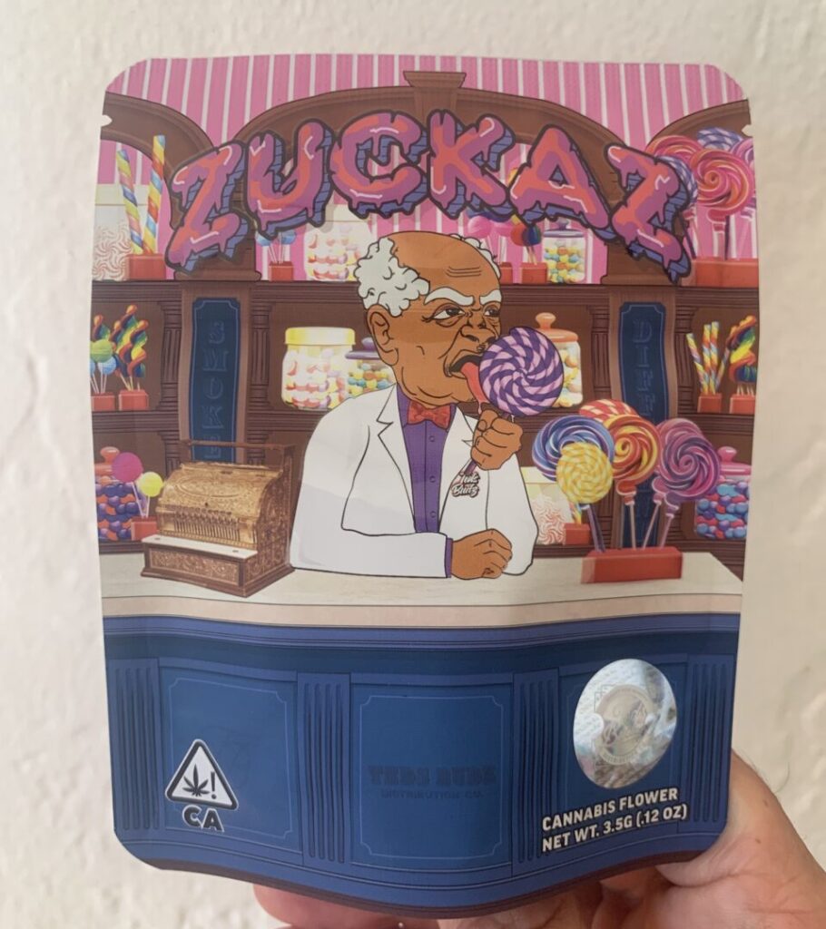 Cannabis package for the “Zuckaz” strain with the cartoon figure of Grandpa Ted behind an old-fashioned candy counter, licking a giant lollypop, with candy-filled wood shelves in the background.