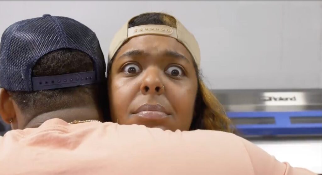 A close up of a woman worker with a look of horror on her face as Lewis embraces her.