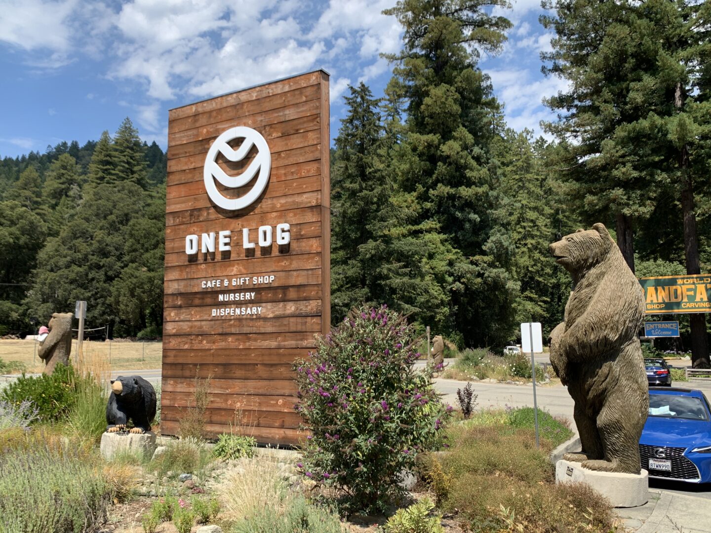 A wooden sign for Berner’s One Log cannabis complex in Humboldt County, flanked by wooden sculptures of bears and surrounded by trees.