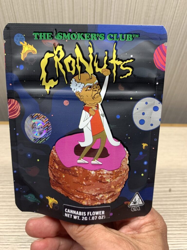 A cartoon image of Theo Lewis’ grandfather and namesake on package for the strain called “Cronuts.” Bald with a horseshoe of grey hair, Grandpa Ted stands on a giant pink glazed cronut in outer space, shaking his fist at the surrounding planets.