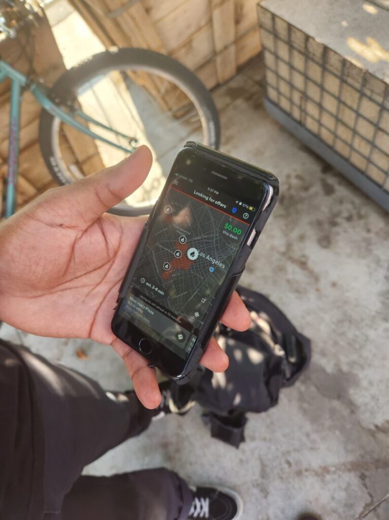 A rider in Los Angeles is holding a smartphone. On the screen we can see the app interface for DoorDash.