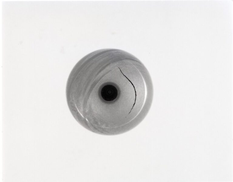 Abstract image in black and white of what resembles a camera aperture surrounded by a gray circle with a crack in it.
