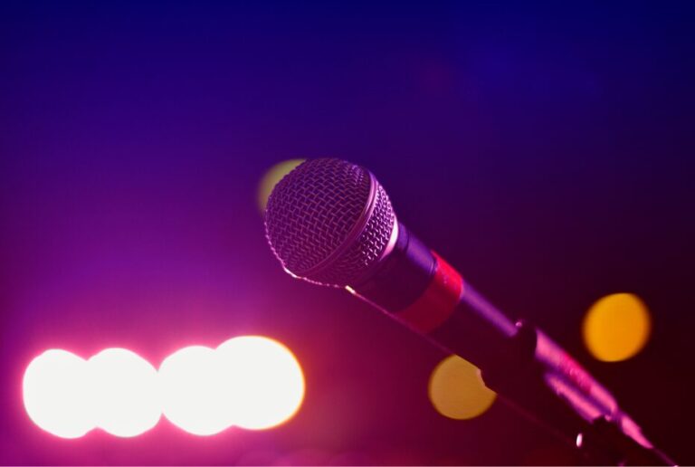 Close-up photo of a microphone with blurred pink lights in the background