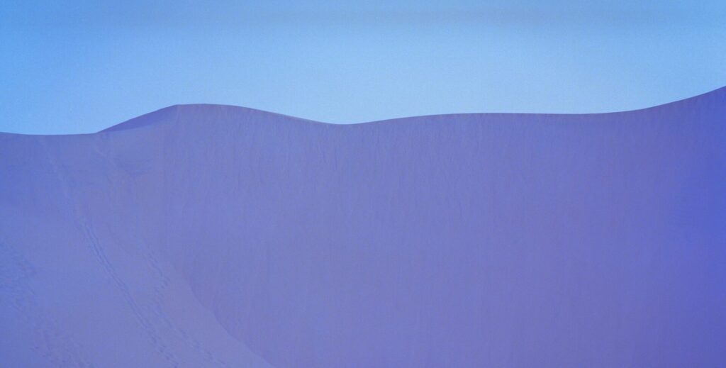 Purple-colored sand dunes against a pale blue sky