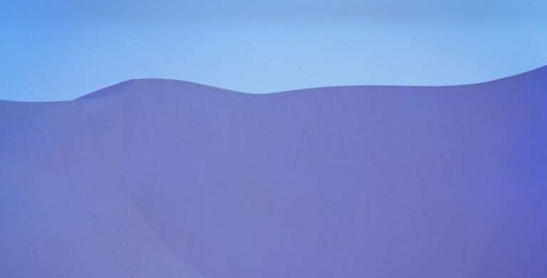 Purple-colored sand dunes against a pale blue sky