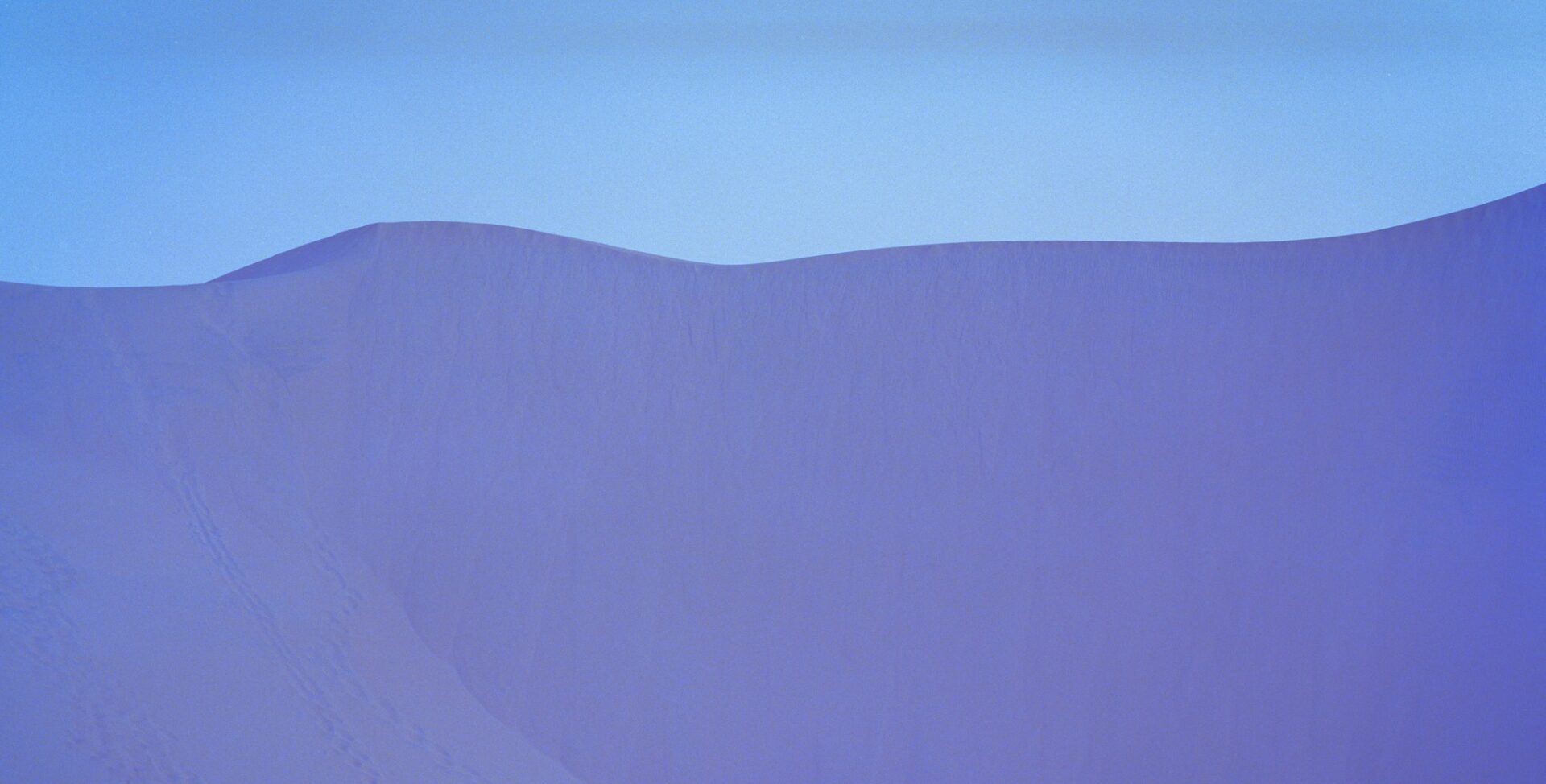 Purple-colored sand dunes against a pale blue sky