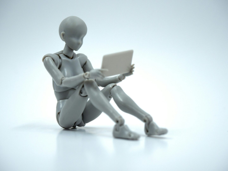 Plastic marionette seated reading a tablet computer.